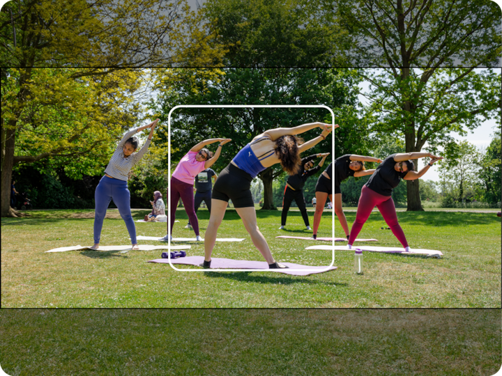 Un groupe de personnes pratiquant le yoga en plein air dans un parc ensoleillé, debout sur des tapis de yoga et faisant des étirements latéraux à l'ombre d'arbres au feuillage vert.