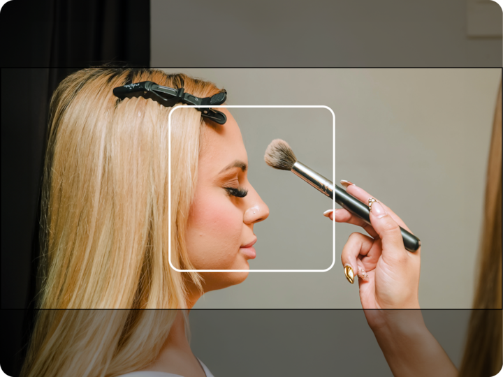 Gros plan de la main d'une maquilleuse appliquant de la poudre sur le côté du visage d'une femme à l'aide d'un pinceau, les cheveux blonds de la femme étant retenus par une pince.