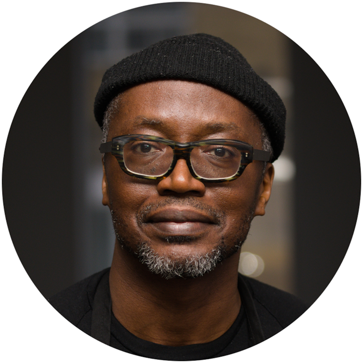 Plan rapproché d'une personne portant un bonnet noir et des vêtements noirs, debout à l'intérieur avec un arrière-plan neutre flou.