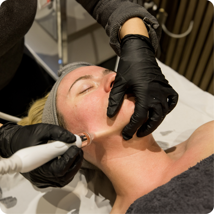 Plan rapproché d'une personne recevant un soin du visage, avec un professionnel portant des gants noirs et utilisant un appareil sur le cou de la personne.