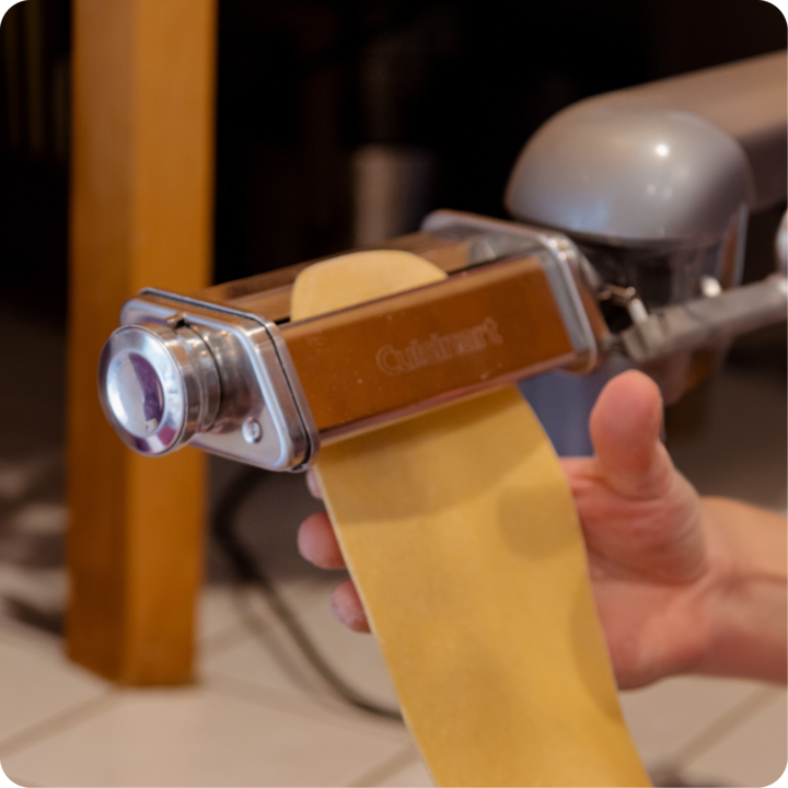 Plan rapproché d'une personne utilisant une machine à pâtes pour étaler des feuilles de pâte fraîche dans une cuisine.