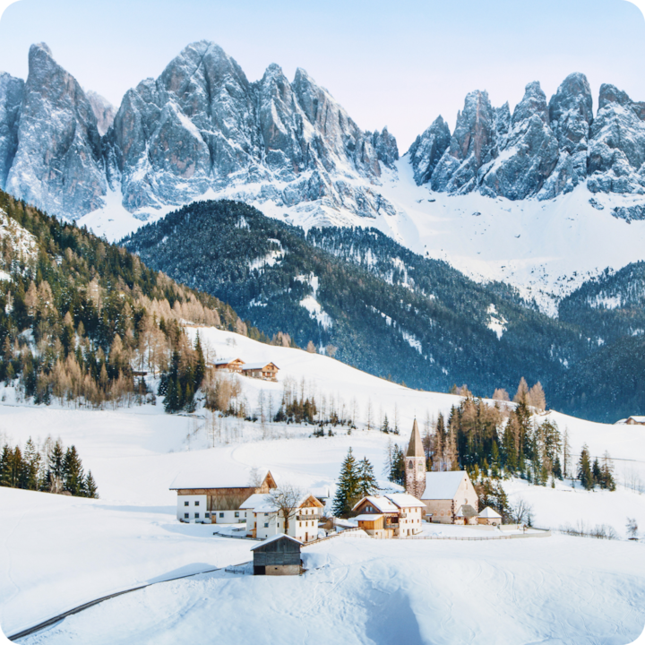 A small, snowy ski village high in the Dolomite mountains with ski slopes in the background