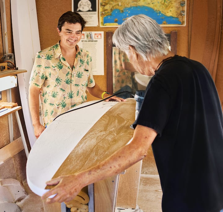 Պատկերում՝ ստուդիայում երկու հոգի աշխատում են սերֆինգի փայտե ձեռագործ տախտակի վրա