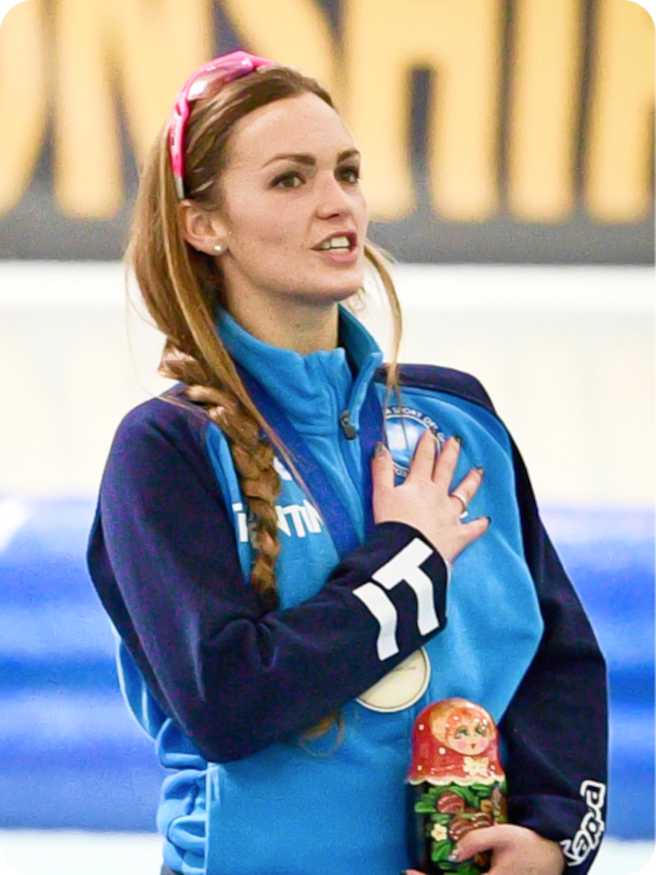 Close shot of Francesca Bettrone during the national anthem wearing a training jacket, one hand over hear heart, the other holding a nesting doll