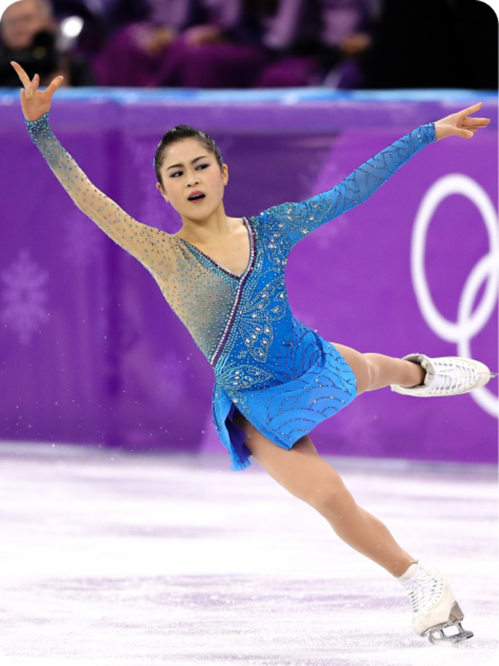 Satoko Miyahara glides across the ice with arms and one leg raised wearing a blue performance outfit