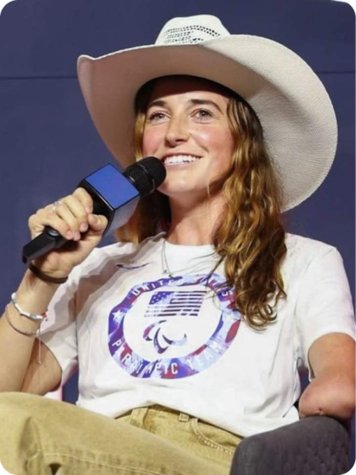 Dani Aravich holds a large microphone while being interviewed. She wears a cowboy hat and oversized t-shirt