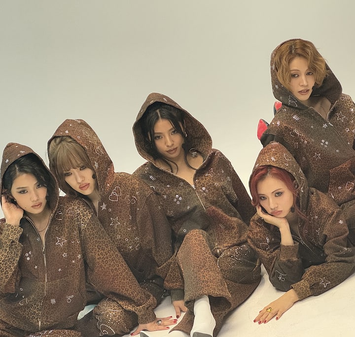 A group of people wearing matching brown leopard-print hooded jumpsuits with scattered star and heart patterns, sitting and posing casually against a neutral backdrop.