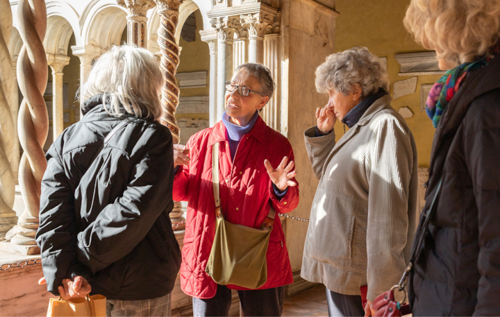 Un groupe de quatre personnes est engagé dans une discussion dans un bâtiment historique aux colonnes de pierre décorées où se diffuse la lumière du soleil.
