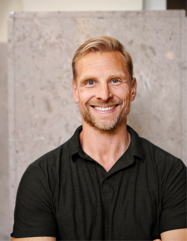 Une personne portant un polo sombre se tient devant un mur de pierre gris clair.