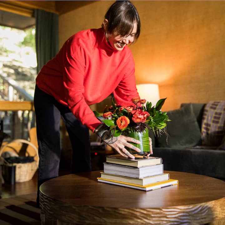 Woman wearing a red sweater sets a vase of flowers on the table