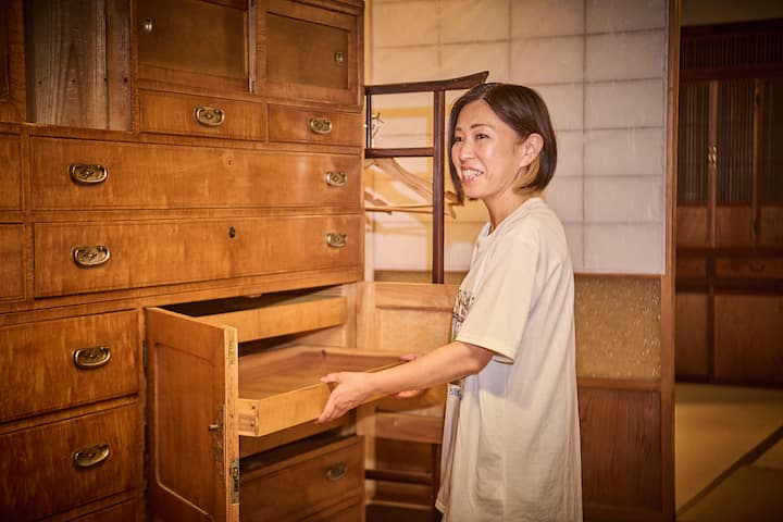 A person opening a wooden drawer in a traditional Japanese-style room with wooden furniture and shoji screens in the background.
