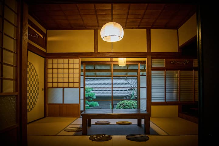 Traditional Japanese tatami room with wooden sliding doors, a low table surrounded by floor cushions, and a paper lantern lighting the space.