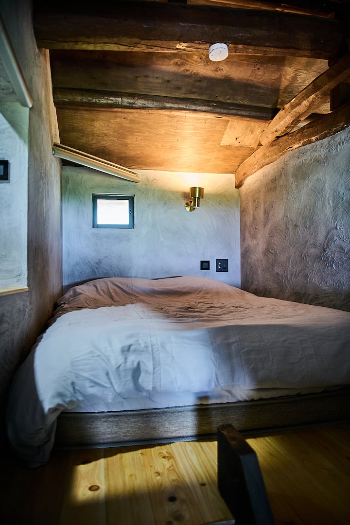A cozy wooden sleeping area with a soft bed, small window, and warm lighting, showcasing traditional Japanese architecture and design.
