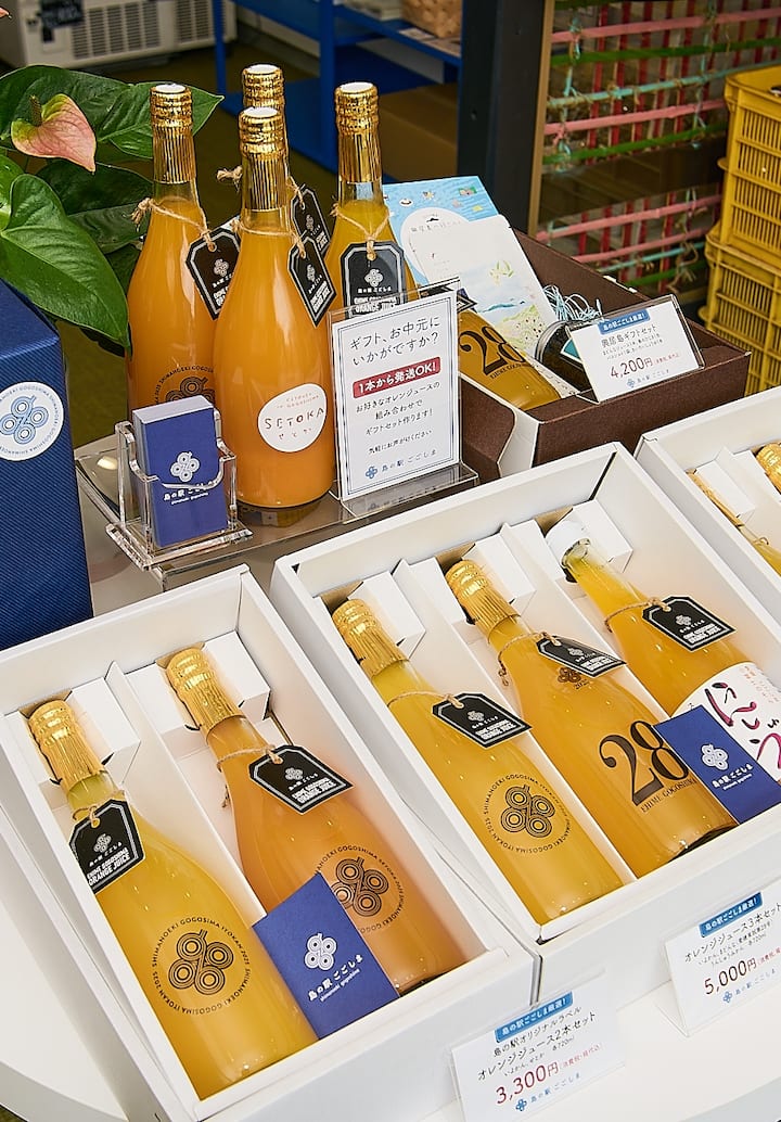 A display of gift sets featuring Japanese orange juice bottles with gold caps, branded tags, and price labels in a shop setting.