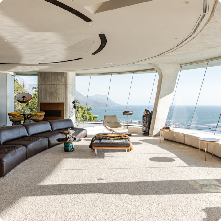 Un salon moderne et ensoleillé avec canapé modulable en cuir, chaise longue, décoration contemporaine et baies vitrées offrant une vue panoramique sur l'océan.