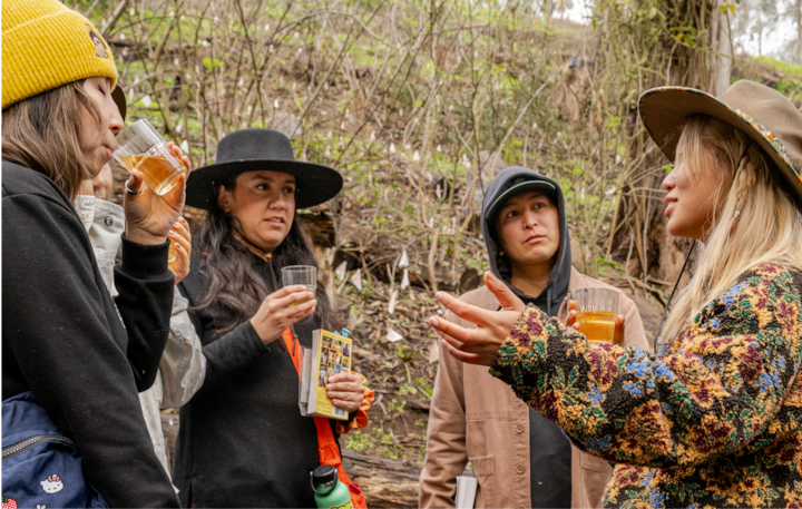 Un groupe de personnes participent à une expérience guidée en plein air. Elles tiennent des boissons et une brochure, entourées de nature et d'arbres.