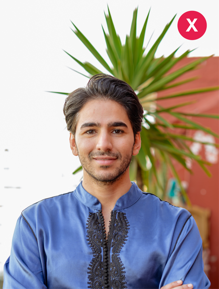 Plan rapproché d'une personne vêtue d'un haut bleu brodé debout devant un mur rouge et une plante verte. Une croix rouge en haut à droite indique que ce type de photo n'est pas un exemple à suivre.