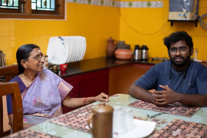 A bright, welcoming kitchen with yellow walls, red cabinets, and a dining table set with placemats, a brass jug, and water glasses, reflecting a homely atmosphere.