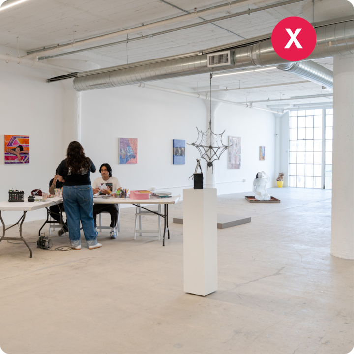 Un grand atelier minimaliste baigné de lumière naturelle grâce à de hautes fenêtres. Des œuvres d'art sont disposées sur les murs et une table centrale permet aux participants d'exprimer leur créativité avec des fournitures d'art.