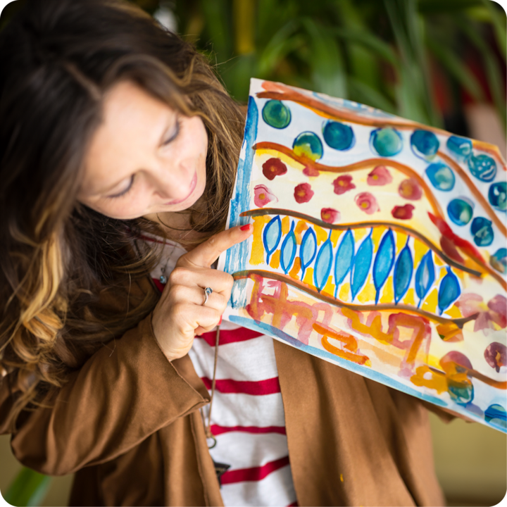 Plan rapproché d'une main pointant vers une œuvre d'art aux couleurs vives, avec des motifs ondulés, des pois et un mélange de tons bleus, jaunes et rouges.