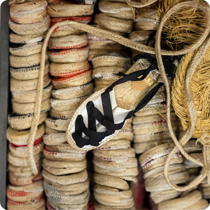 Une paire d'espadrilles à lacets noirs se démarque parmi des rangées de semelles tissées, mettant en valeur un produit fini d'un atelier local.