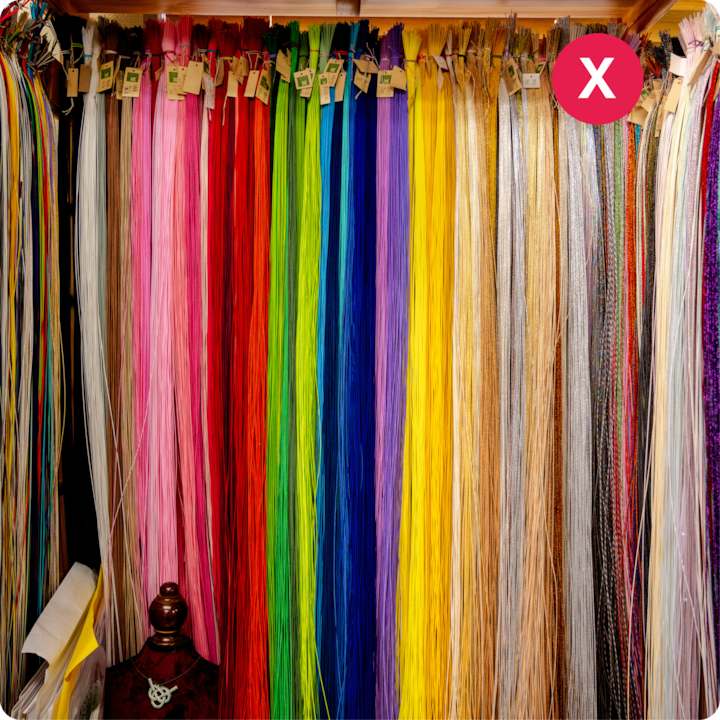 Un assortiment de fils de différentes couleurs vives, suspendus soigneusement sur une étagère, avec un « X » blanc sur fond rouge dans le coin suggérant qu'il s'agit d'un exemple à éviter.