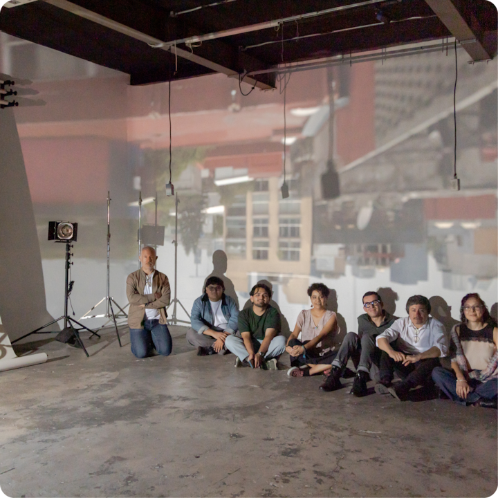 Un groupe de personnes est assis sur le sol d'un atelier baigné d'une lumière douce et diffuse. Un paysage urbain est projeté sur le mur derrière elles, créant une atmosphère créative et immersive.