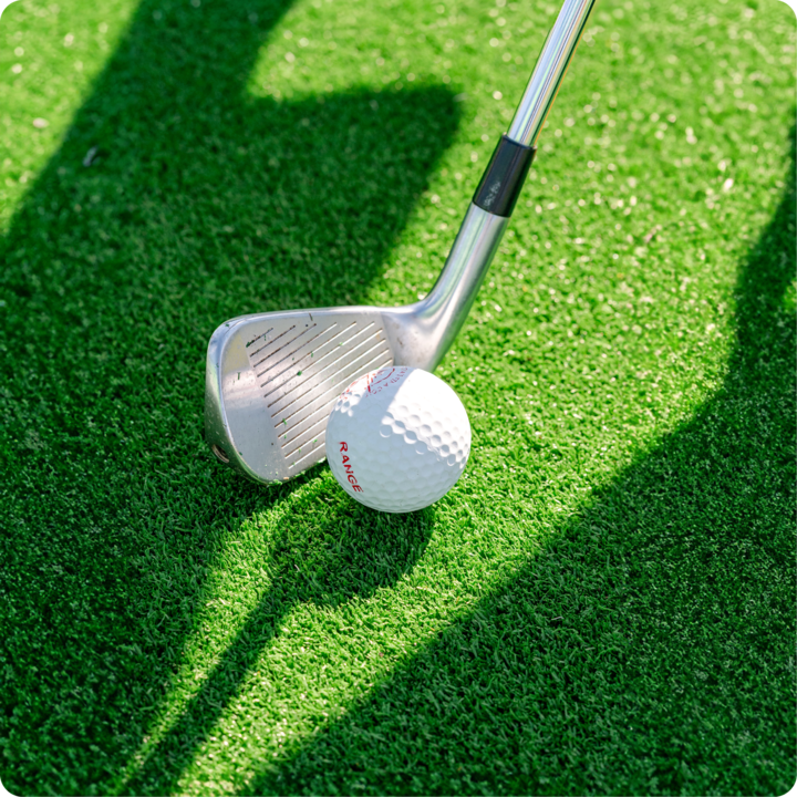 Un plan rapproché d'un club de golf placé à côté d'une balle de golf sur un gazon vert vif, avec les ombres d'objets à proximité.