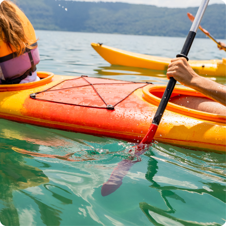 Plan rapproché d'une personne pagayant sur un kayak jaune et orange sur une eau calme et claire entourée de collines verdoyantes.
