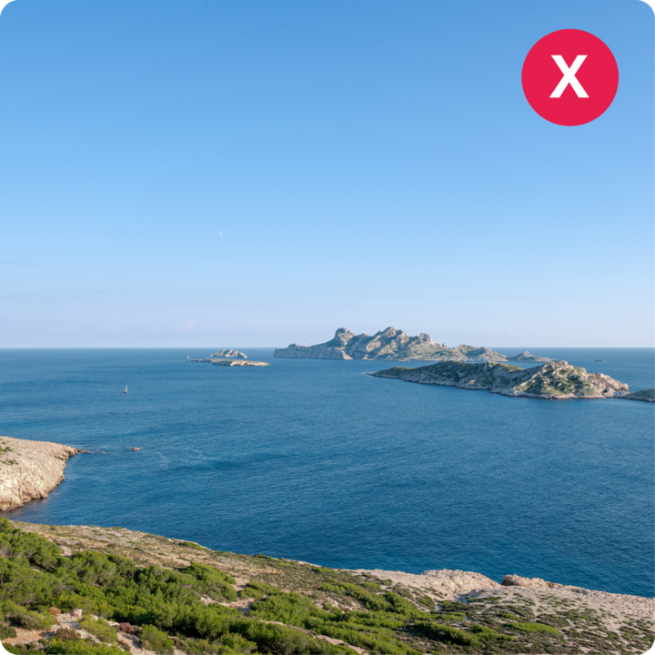 Une vue panoramique sur un océan bleu calme avec des petites îles rocheuses au loin sous un ciel bleu limpide.