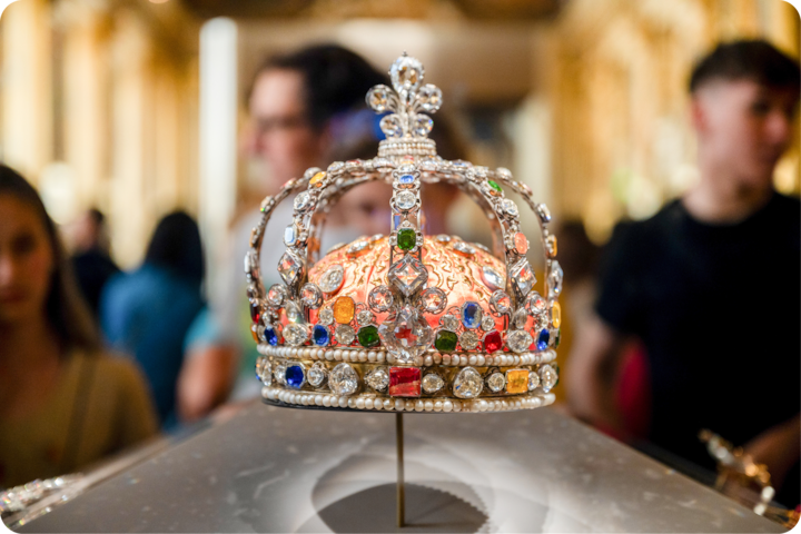 Une couronne ornée de pierres précieuses multicolores, de détails complexes et d'une base dorée, présentée dans un musée bien éclairé.