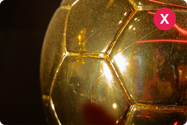 Une vue détaillée d'un trophée de football doré reflétant la lumière. Dans le coin supérieur droit, un cercle rouge avec en son centre un X est superposé sur la photo.