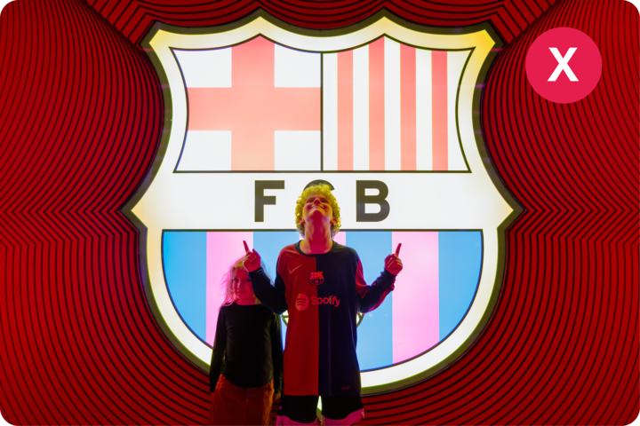 L'écusson lumineux du FC Barcelone en arrière-plan, avec deux personnes debout devant, vêtues de vêtements sombres, sur un motif circulaire rouge vif.