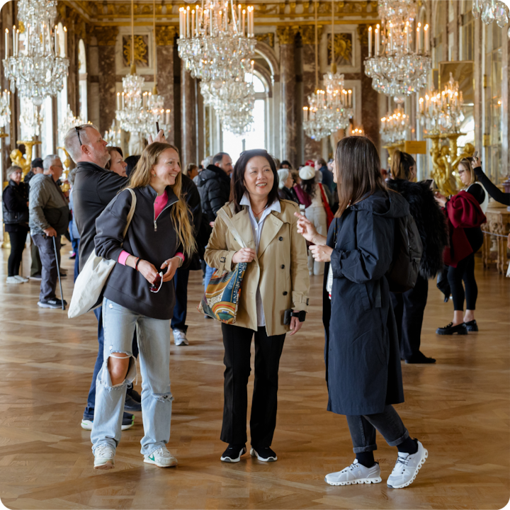 Un groupe de personnes dans une salle somptueuse avec des lustres en cristal et des touches dorées opulentes, discutant au milieu des visiteurs du musée.