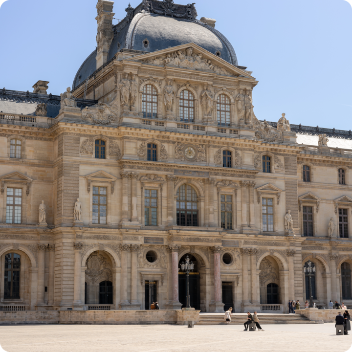 La façade emblématique du musée du Louvre à Paris, avec des sculptures détaillées, des statues et une horloge centrale, ainsi qu'une vaste cour au premier plan.