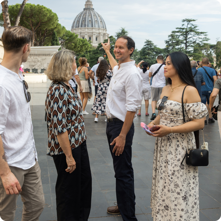 Un groupe de visiteurs discute près du dôme de la basilique Saint-Pierre, tandis que d'autres touristes explorent les environs sous un ciel nuageux.