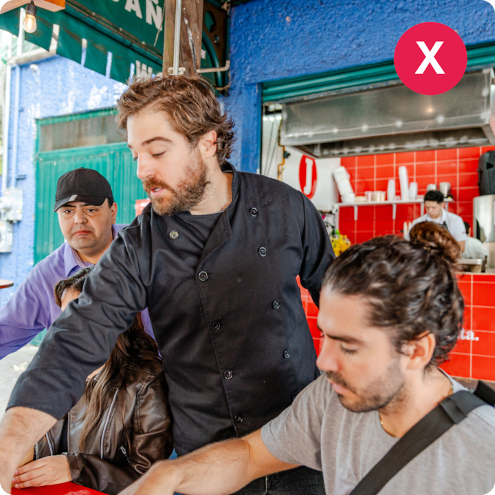 Un stand de nourriture animé avec un chef en veste noire servant un groupe de convives près d'un comptoir avec des carreaux rouges et des ustensiles de cuisine.