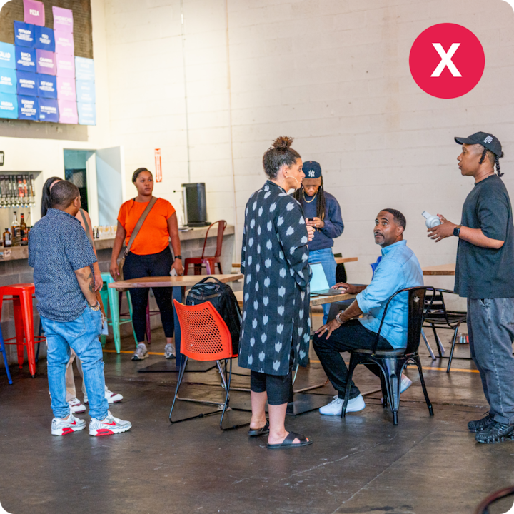 Une scène en intérieur avec des personnes discutant près d'une table, entourée de sièges colorés et d'un espace bar, évoquant une ambiance conviviale et accueillante.