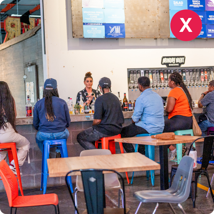 Un groupe de personnes rassemblées dans un bar avec des bouteilles et des tireuses participent à une séance de découverte gastronomique dirigée par un hôte.