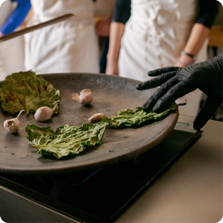 Une personne portant des gants noirs fait cuire de la laitue et de l'ail dans une poêle.