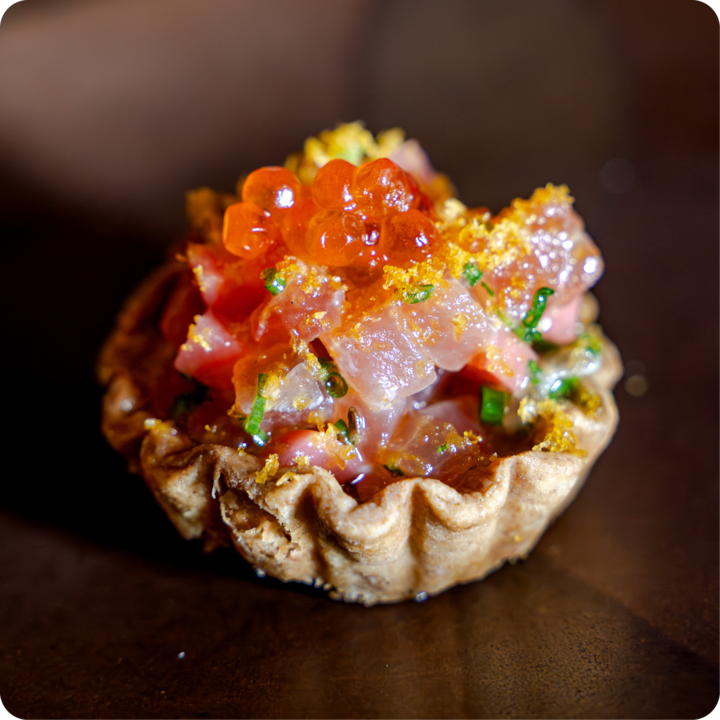 Tarte gastronomique avec des garnitures colorées, notamment des dés de poisson, des herbes et des œufs de poisson orange vif, mettant en valeur le produit final d'un voyage culinaire unique.
