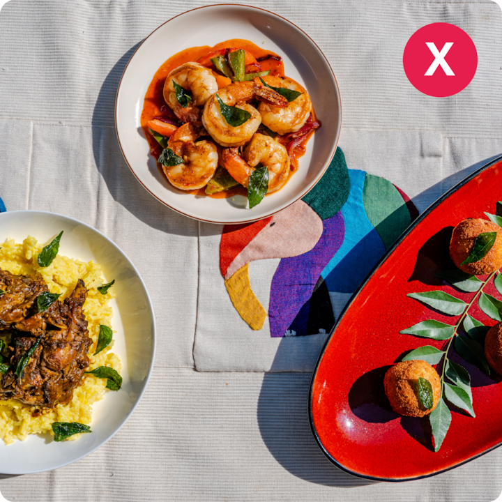 Un assortiment de plats savoureux, notamment du curry de crevettes, du riz jaune avec de la viande épicée et des boulettes frites croustillantes, présentés sur une nappe lumineuse avec un motif d'oiseau coloré, mettant en valeur la culture culinaire locale.