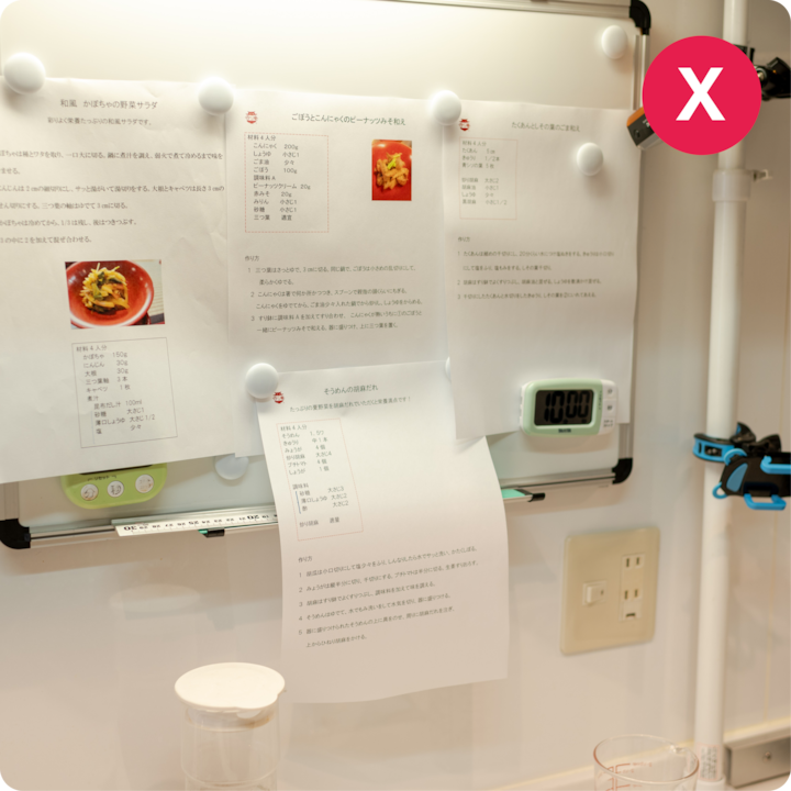 Un tableau blanc de cuisine avec des feuilles de recettes imprimées et épinglées, montrant des instructions de cuisson détaillées et des images de plats préparés, à côté d'une minuterie indiquant 10 h 00.