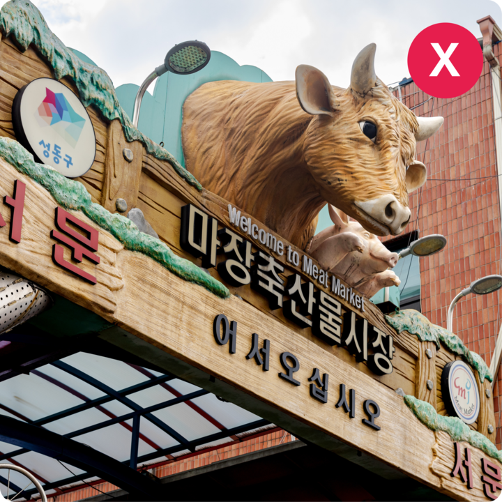 Une enseigne d'un marché de viande est affichée sous des sculptures de vache et de cochon, avec du texte en anglais et en coréen contre une arche en bois.