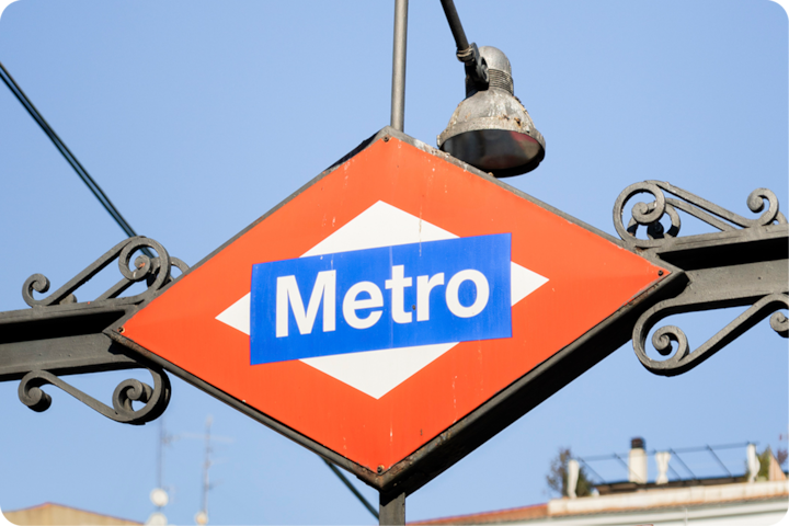Un gros plan d'un panneau rouge et blanc du métro de Madrid avec « Metro » écrit en lettres blanches sur fond bleu, sur un ciel bleu dégagé.