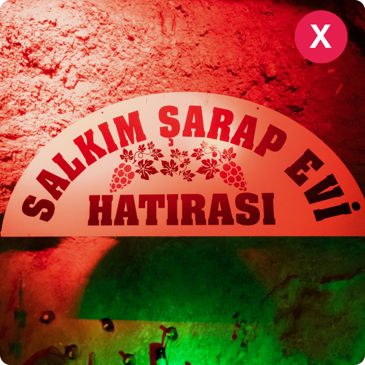 Un panneau en forme d'arche avec le texte « Salkım Şarap Evi Hatırası » et des motifs de raisins, posé sur un mur de pierre éclairé en rouge.