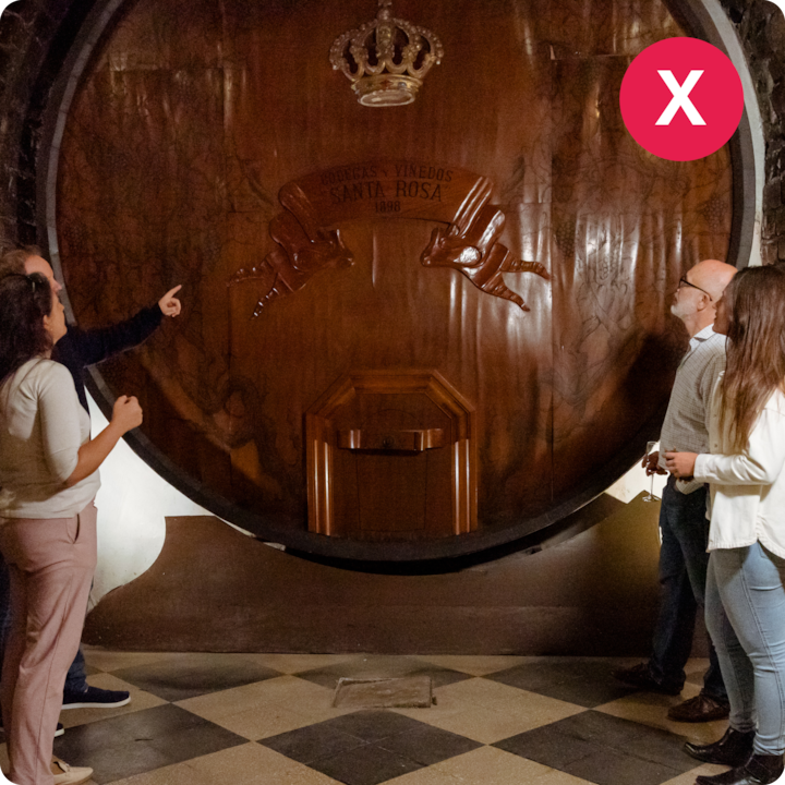 Quatre adultes sont rassemblés pour une dégustation à côté d'un énorme tonneau de vin en bois avec des sculptures raffinées et une couronne gravée.