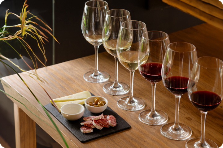 Un plan rapproché d'une présentation de dégustation avec six verres de vin rouge et blanc à côté d'une planche en ardoise garnie de fromage, d'olives, de salami et de sauces sur une table en bois rustique.