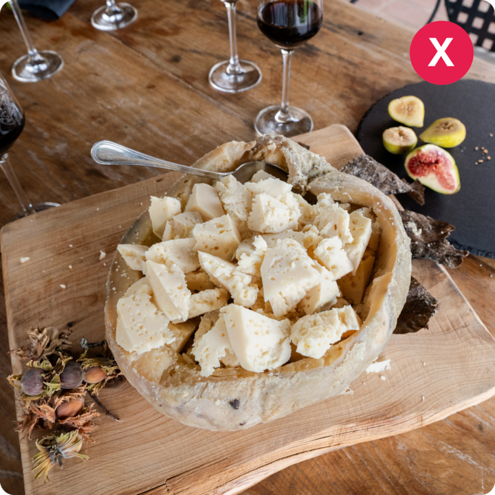 Un plan rapproché d'une croûte de fromage remplie de morceaux de fromage sur une table en bois rustique, à côté de verres de vin rouge et de figues fraîches, pour montrer un exemple de présentation culinaire.