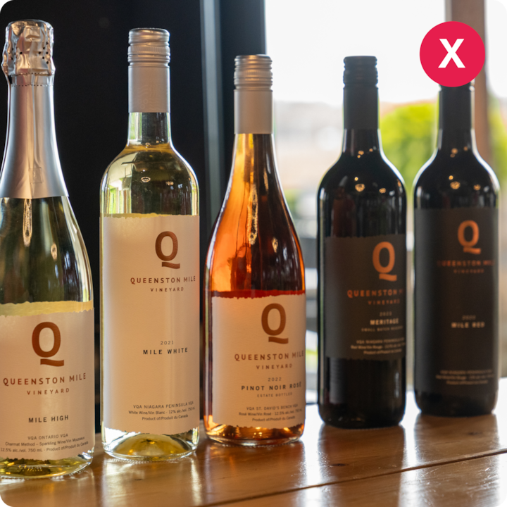 Une rangée de bouteilles de vin du vignoble Queenston Mile, dont du mousseux, du blanc, du rosé et du rouge, sur une table en bois.